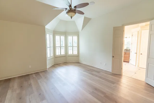 an empty room with wooden floor fan and windows