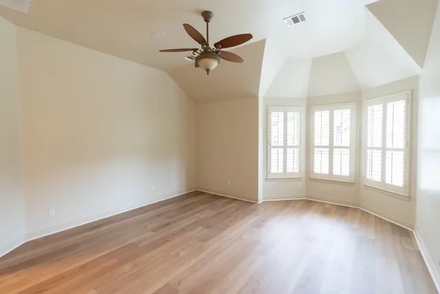 an empty room with wooden floor fan and windows