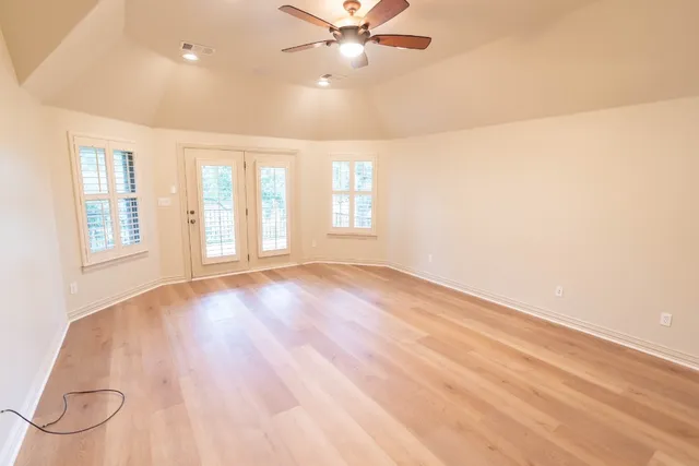 an empty room with wooden floor fan and windows
