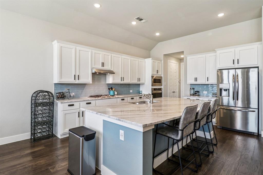 847 Longbranch Way Little Elm, TX 76227 - Photo 9 of 39 Kitchen featuring appliances with stainless steel finishes, decorative backsplash, lofted ceiling, white cabinetry, and light stone countertops