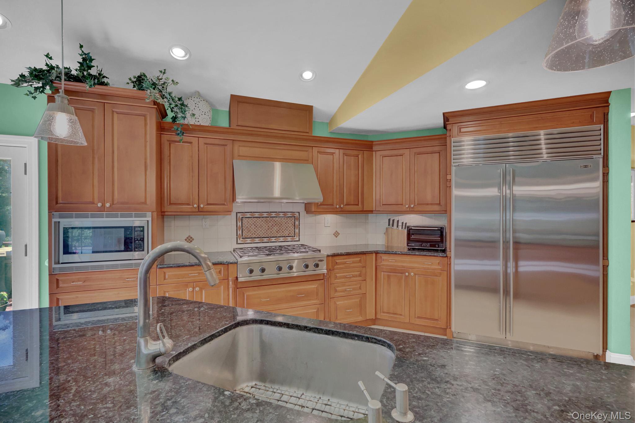 15 Stillwater Road Nissequogue, NY 11780 - Photo 11 of 43 Kitchen featuring rich wood cabinetry, patterned backsplash tile, stainless steel appliances, and dark speckled countertops