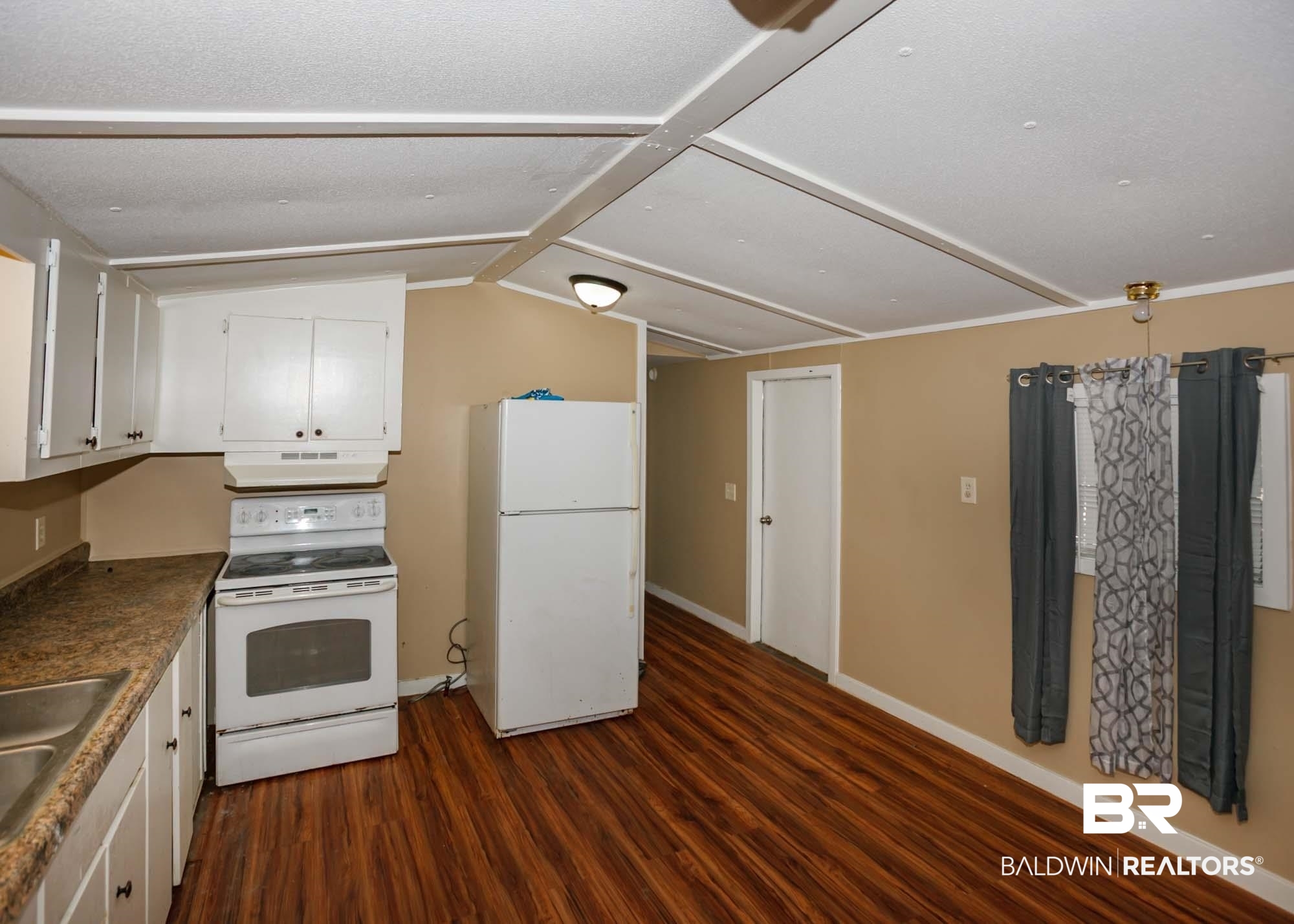 11998 Workman Avenue Foley, AL 36535 - Photo 37 of 59 Kitchen featuring white appliances, dark wood-style floors, white cabinets, under cabinet range hood, and vaulted ceiling