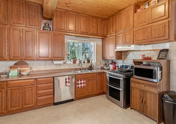 a large kitchen with stainless steel appliances granite countertop a refrigerator a sink dishwasher a stove and a refrigerator with wooden cabinets