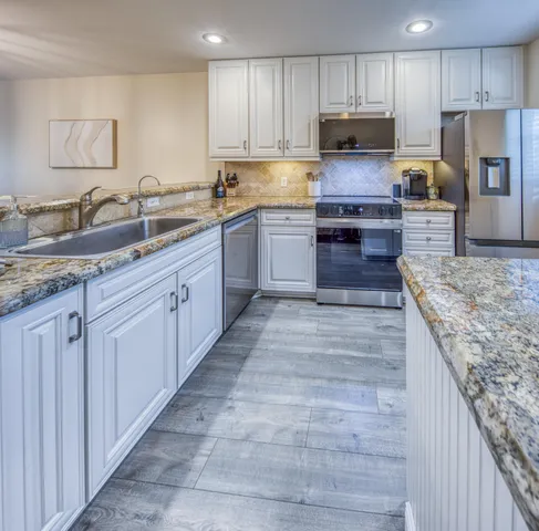 a large kitchen with granite countertop a stove top oven a sink dishwasher and a refrigerator with wooden cabinets