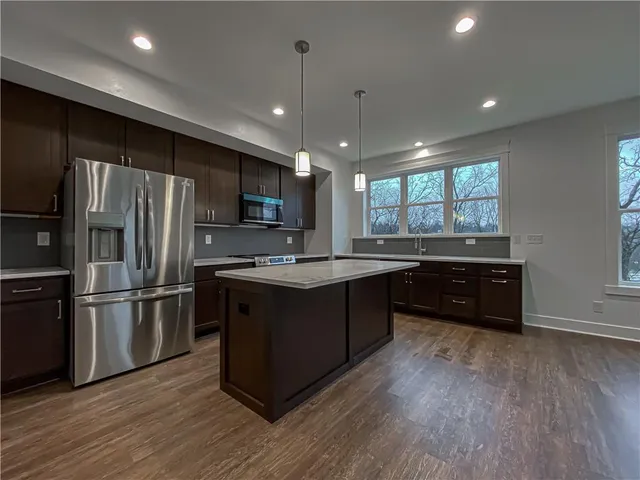 a kitchen with stainless steel appliances granite countertop a refrigerator a sink dishwasher a stove and a microwave oven on wooden floor