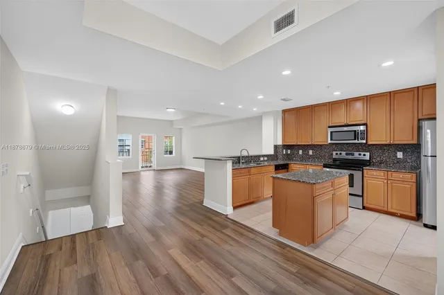 a kitchen with stainless steel appliances granite countertop a refrigerator a sink dishwasher and a stove with wooden floor