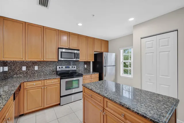 a kitchen with stainless steel appliances granite countertop a stove a sink and a refrigerator with wooden cabinets