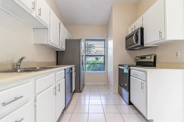 a kitchen with granite countertop white cabinets stainless steel appliances a sink and a window
