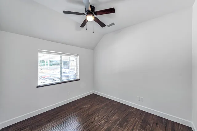 an empty room with wooden floor ceiling fan and windows