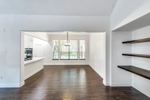 a view of a kitchen and an empty room with wooden floor and a window