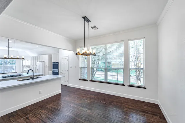 a large kitchen with granite countertop a stove a sink and white cabinets with wooden floor