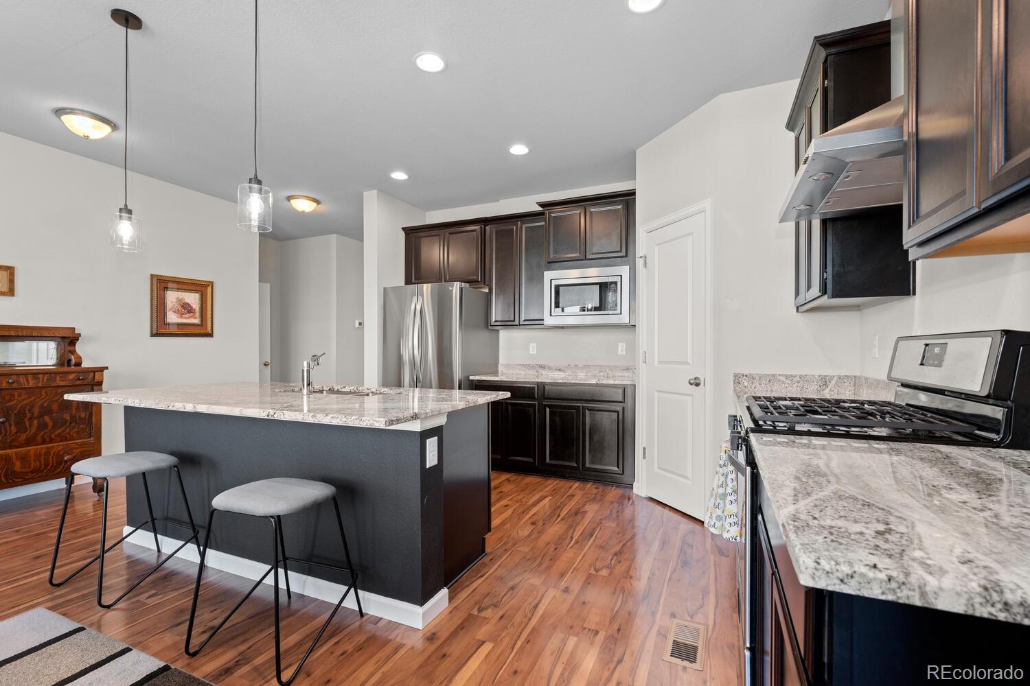 1587 Lake Point Way Severance, CO 80550 - Photo 17 of 40 a kitchen with stainless steel appliances granite countertop a stove top oven a sink dishwasher a dining table and chairs with wooden floor