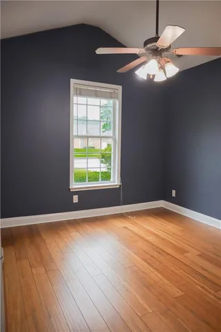 an empty room with wooden floor fan and windows