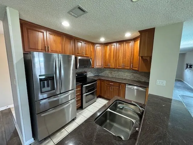 a kitchen with granite countertop stainless steel appliances a refrigerator stove top oven and sink