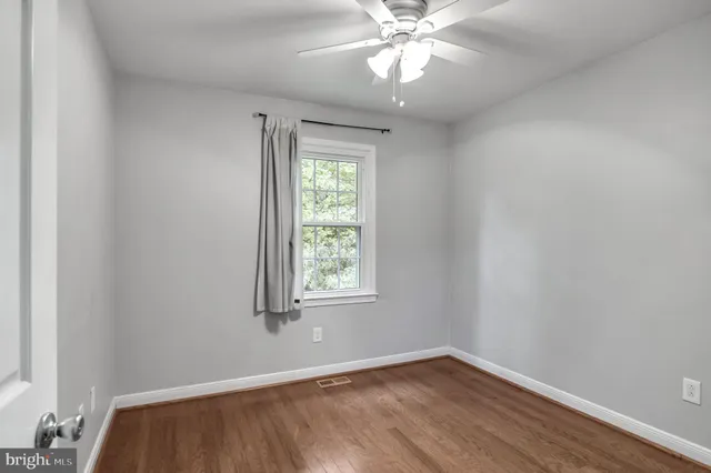 an empty room with wooden floor chandelier fan and windows