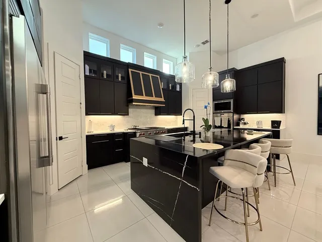 a kitchen with stainless steel appliances kitchen island granite countertop a refrigerator a sink a stove and chairs with wooden floor