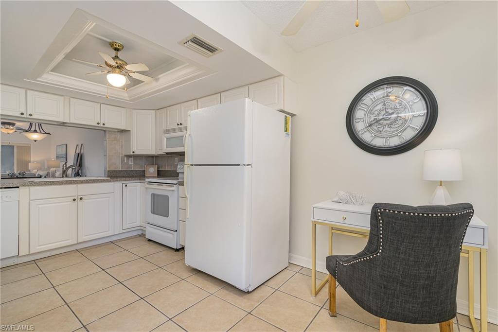 5535 Rattlesnake Hammock Road, Unit 103 Naples, FL 34113 - Photo 7 of 25 Kitchen featuring white appliances, a raised ceiling, ceiling fan, white cabinetry and extra space to curate an office or use for kitchen table.