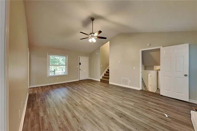 an empty room with wooden floor chandelier fan and windows