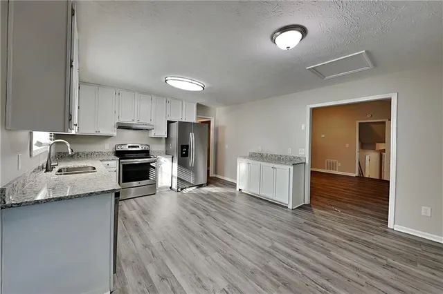 a kitchen with stainless steel appliances granite countertop a refrigerator a sink dishwasher a stove and white countertops with wooden floor