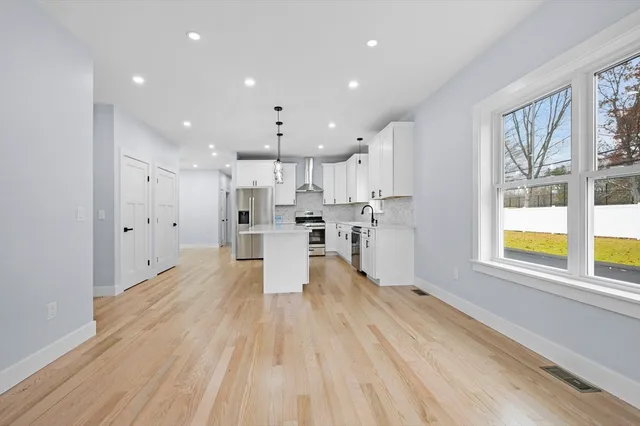 a large white kitchen with stainless steel appliances kitchen island granite countertop a large window and a refrigerator