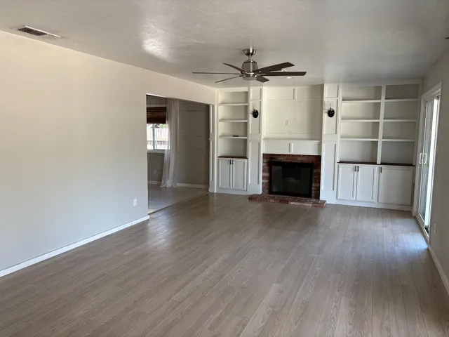 an empty room with wooden floor a ceiling fan and fireplace