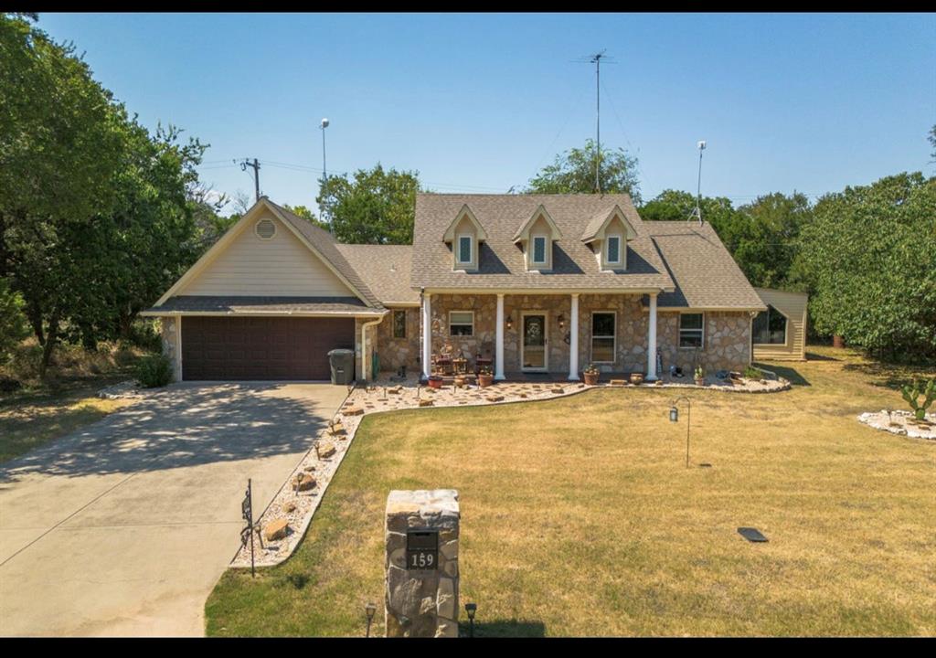 Cape cod-style house with stone siding, covered porch, concrete driveway, an attached garage, and roof with shingles