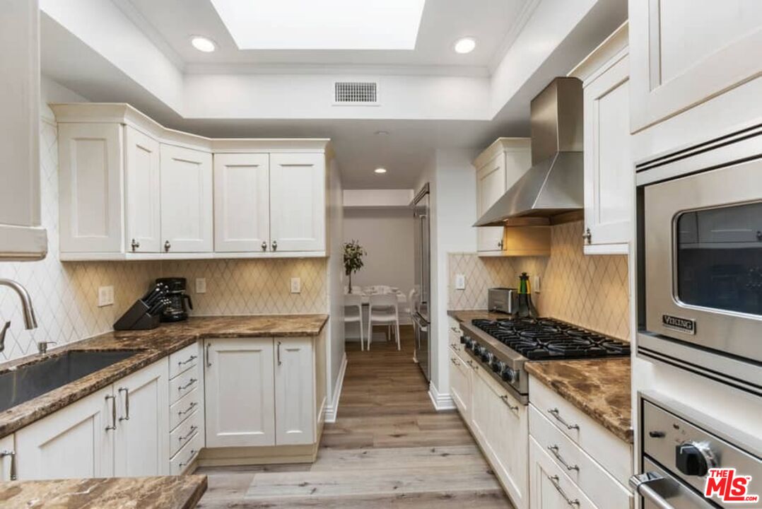 261 South Reeves Drive Beverly Hills, CA 90212 - Photo 12 of 43 a kitchen with stainless steel appliances granite countertop a stove top oven a sink dishwasher and cabinets with wooden floor