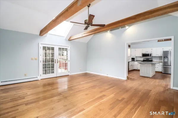 a view of an empty room with wooden floor and a kitchen