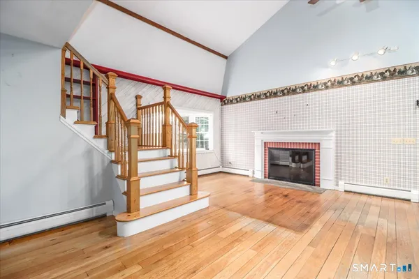 a view of an empty room with wooden floor fireplace and a window