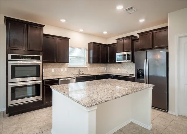 a kitchen with stainless steel appliances granite countertop a refrigerator a stove a sink and a microwave