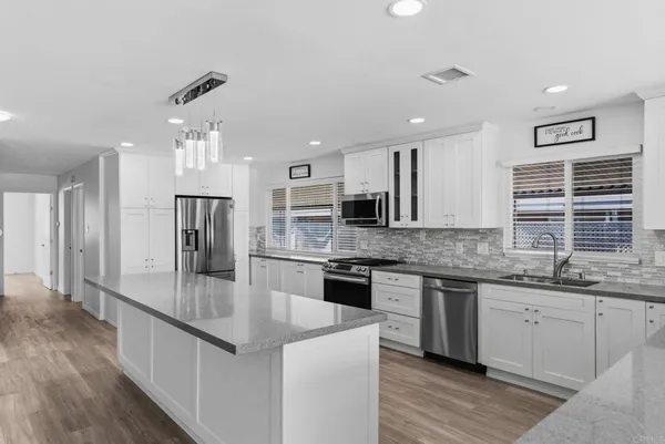 a large kitchen with stainless steel appliances granite countertop a stove top oven a sink dishwasher a refrigerator and white cabinets with wooden floor