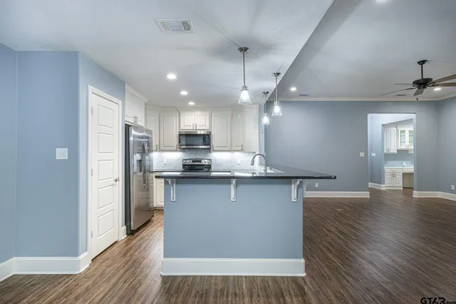 a kitchen with stainless steel appliances granite countertop a refrigerator a sink dishwasher a stove and white countertops with wooden floor