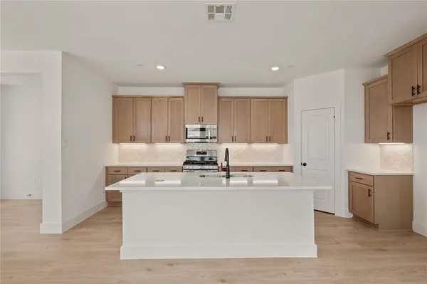 a large white kitchen with stainless steel appliances granite countertop a stove a sink a refrigerator and white cabinets