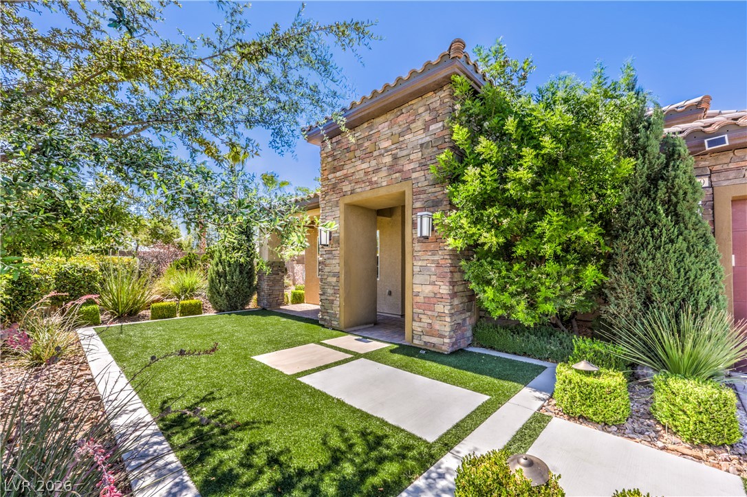 7119 Arabian Ridge Street Las Vegas, NV 89131 - Photo 65 of 73 A welcoming front entrance is framed by stone accents, lush landscaping, and a well-kept lawn.