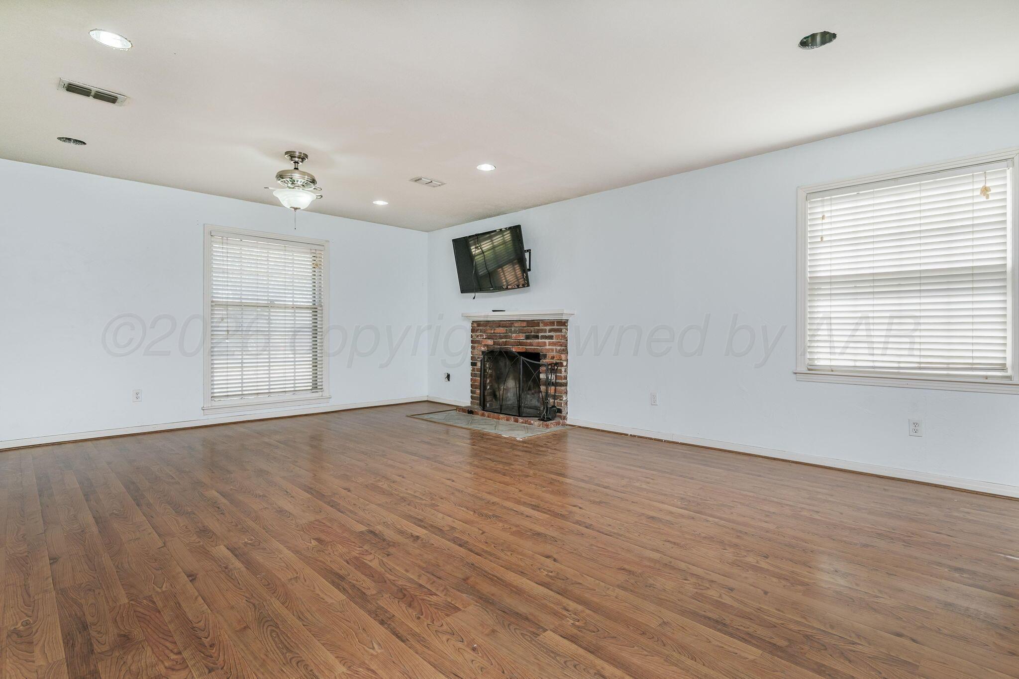 5305 Randolph Road Amarillo, TX 79106 - Photo 4 of 20 an empty room with wooden floor fireplace and windows