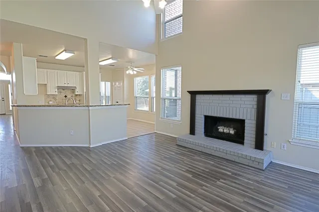 a view of a kitchen and an empty room with wooden floor and a fireplace