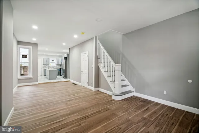 a view of an empty room with wooden floor and kitchen
