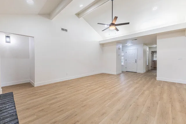 an empty room with wooden floor ceiling fan and windows