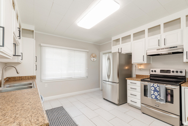 227 West 200 North Logan, UT 84321 - Photo 15 of 44 Kitchen featuring white cabinetry with black hardware, stainless steel appliances, speckled countertops, and light-toned tile flooring