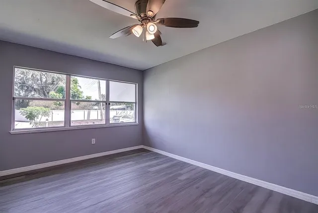 an empty room with wooden floor fan and windows
