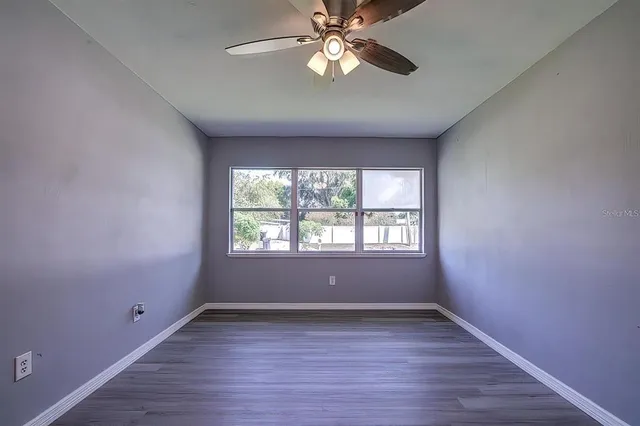 an empty room with wooden floor chandelier fan and windows