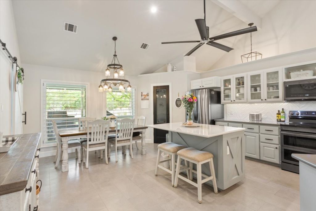 190 Young Ranch Road Georgetown, TX 78633 - Photo 6 of 40 Dual tone kitchen featuring stainless steel appliances, glass fronted cabinets, a kitchen island, a kitchen breakfast bar, and vaulted ceiling