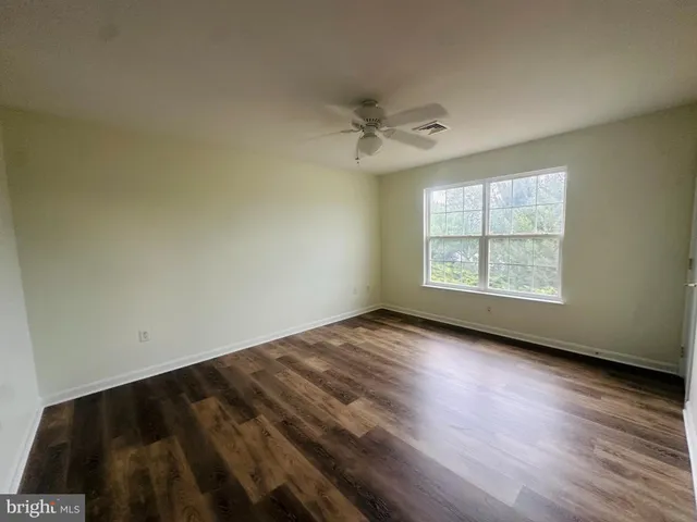 an empty room with wooden floor ceiling fan and windows