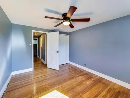 a view of an empty room with wooden floor and a ceiling fan