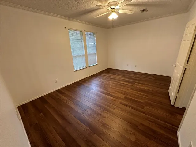 a view of an empty room with wooden floor and a ceiling fan