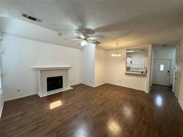 a view of an empty room with wooden floor and a kitchen