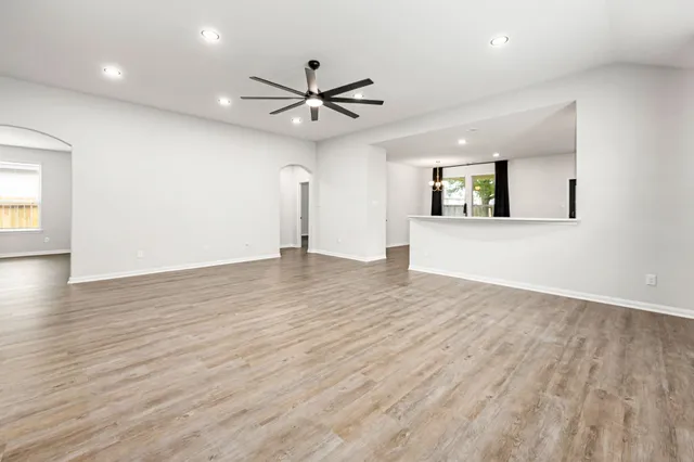 an empty room with wooden floor a ceiling fan and windows