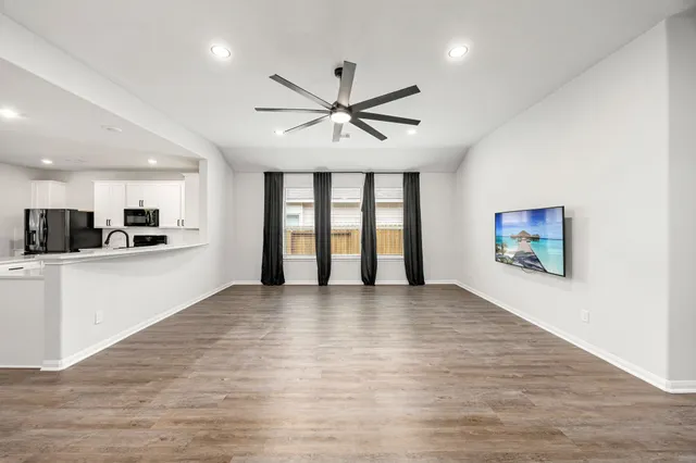 a view of an empty room with window and kitchen view