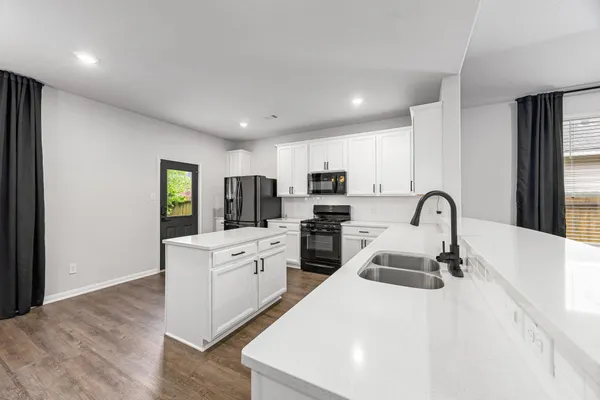 a kitchen with stainless steel appliances a sink a stove top oven a refrigerator with white cabinets and wooden floor