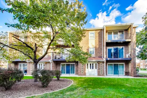 a view of a brick house with a yard plants and a large tree